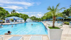 Une piscine avec des chaises longues, des palmiers et une fontaine.
