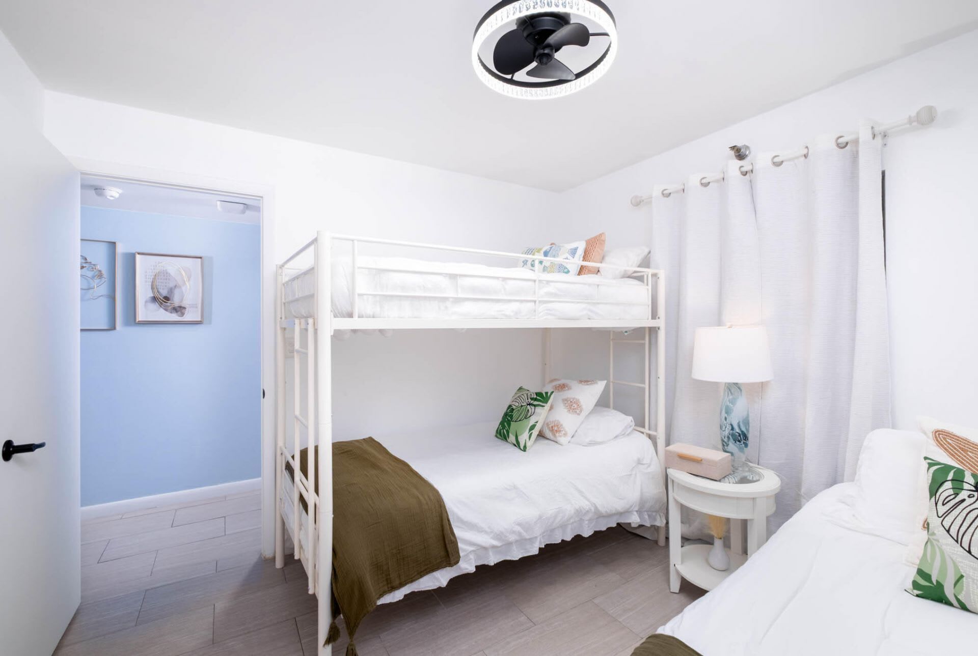 Habitación con literas, ventilador de techo, mesita de noche con lámpara y puerta con un marco de fotos.