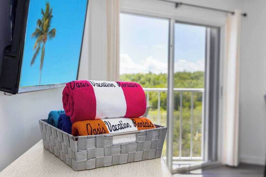 A basket with towels labeled 'Oasis Vacation Rentals' on a balcony with a view of greenery.