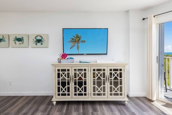 Una habitación con una pared blanca, un mueble de madera con puertas de cristal y un cuadro con una palmera.