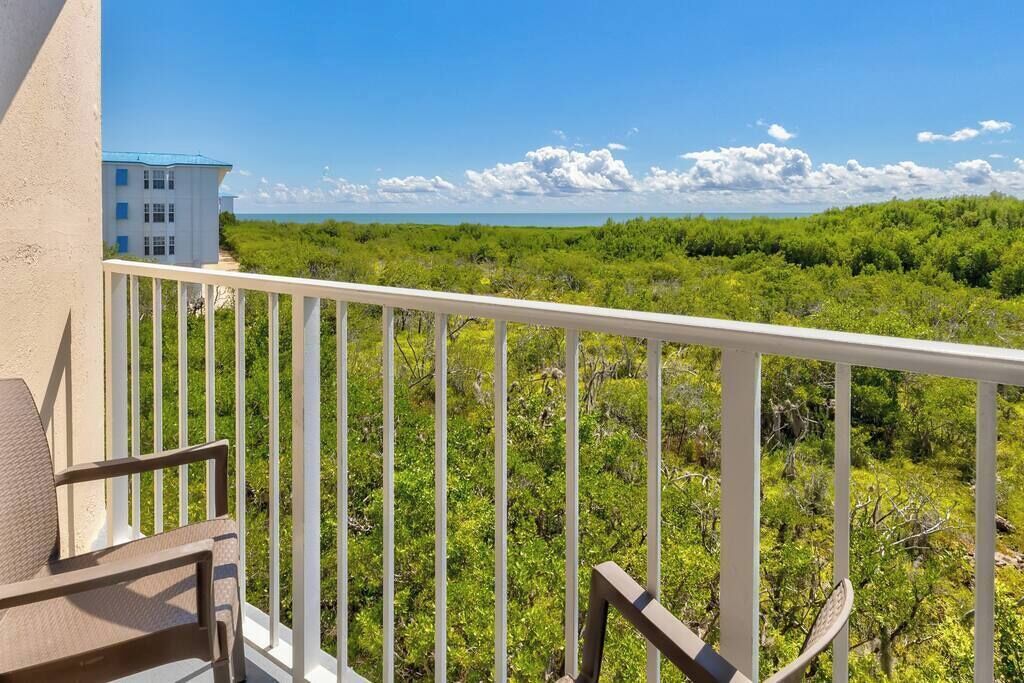 A balcony with a white railing, a chair, and a view of a building and lush greenery.
