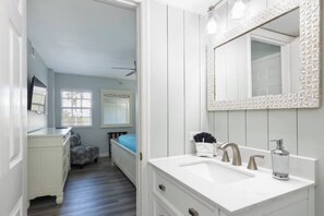 Un baño con tocador blanco, un espejo grande y una cama al fondo.