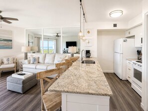 A modern kitchen with a central island, white cabinetry, and a dining area with a sofa and ottoman.