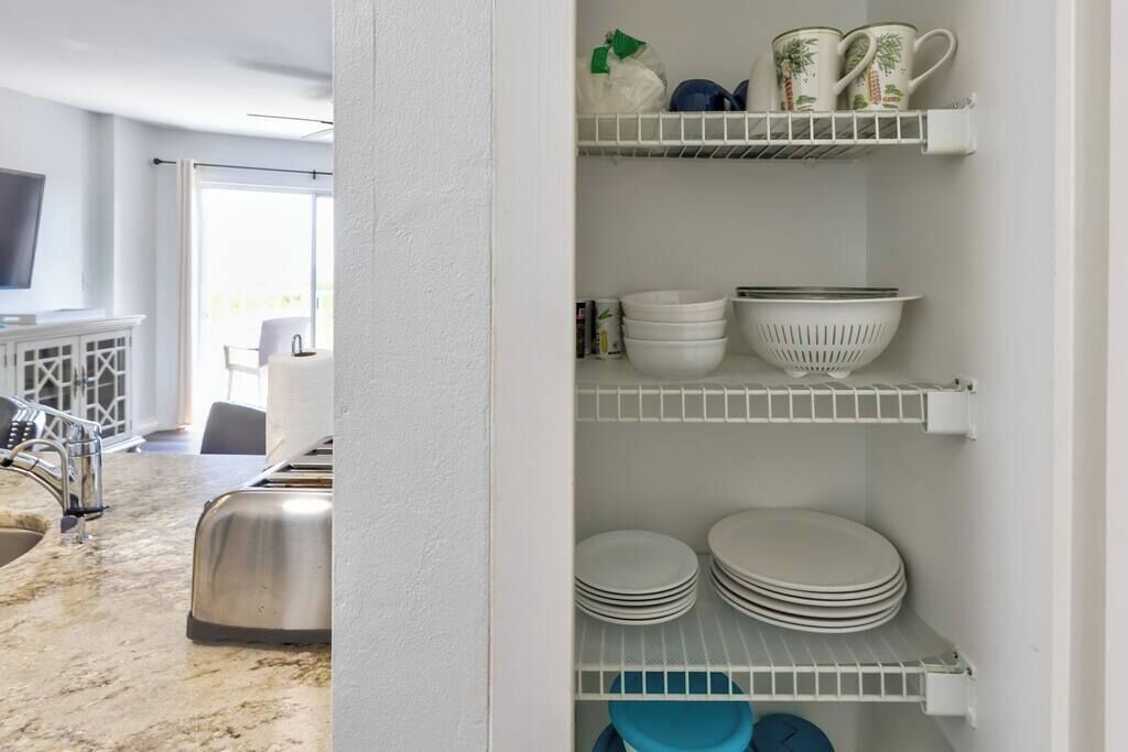 A kitchen with white shelves holding plates, bowls, and cups.