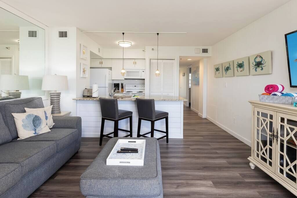 A modern living room with a grey sofa, a coffee table, and a kitchen in the background.