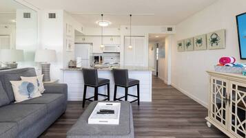 A modern living room with a grey sofa, a coffee table, and a kitchen in the background.
