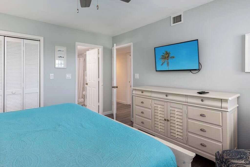 A bedroom with a bed, a dresser, a television, and a door leading to another room.