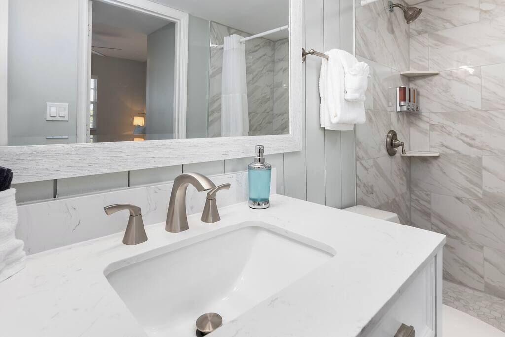 Une salle de bain moderne avec un lavabo blanc, deux robinets, un grand miroir et un espace douche.