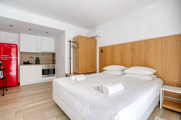 Ein modernes Hotelzimmer mit einem großen Bett, einem Holzkopfstück, einem roten Kühlschrank, einer Küchenzeile und einem Holzboden.