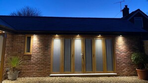 Une maison avec une façade en briques, une grande porte-fenêtre coulissante et un petit jardin agrémenté de plantes en pot.