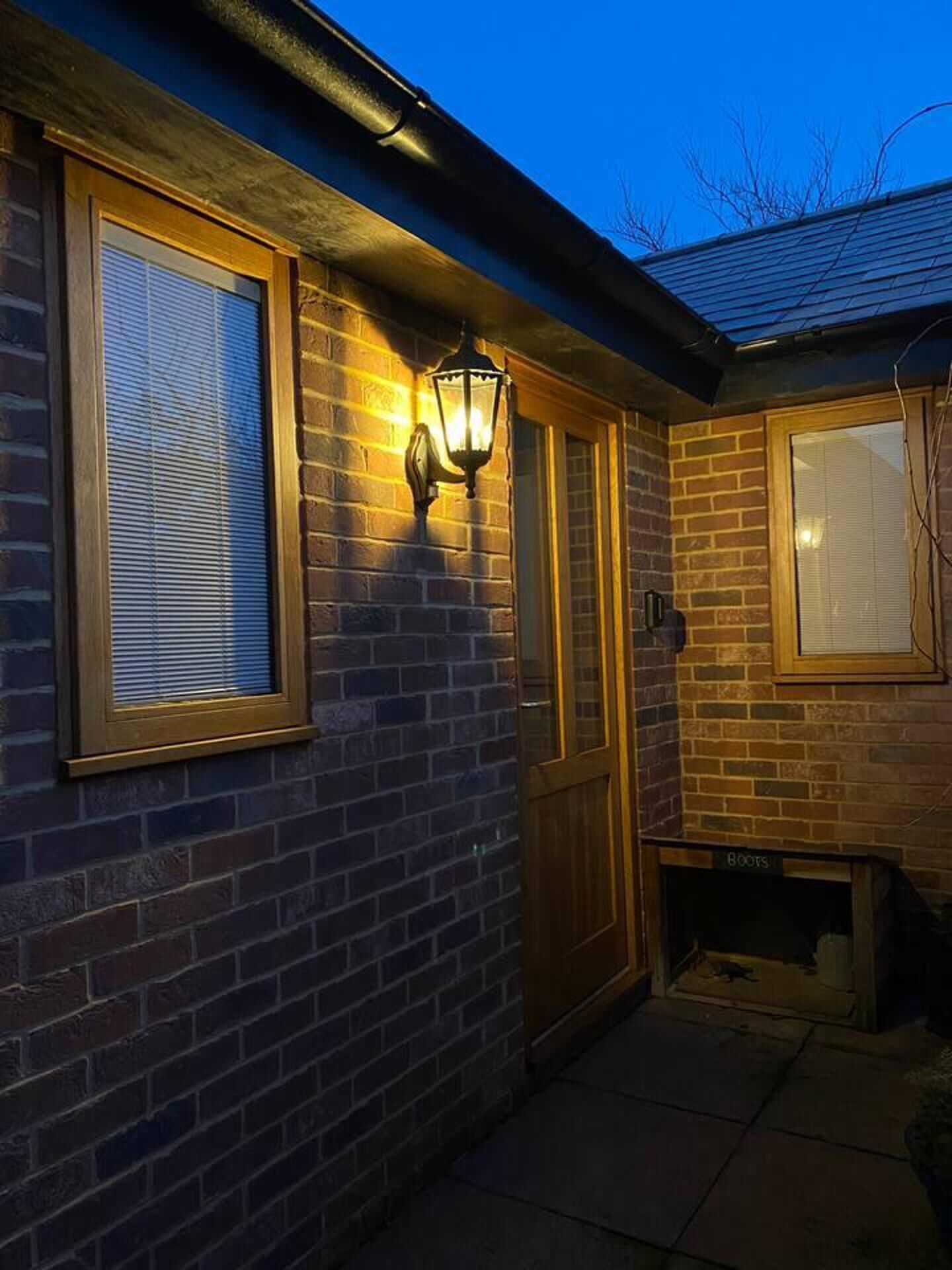 A brick building with a wooden door and windows, a lantern-style light fixture, and a small covered area with a sign reading "Boots".