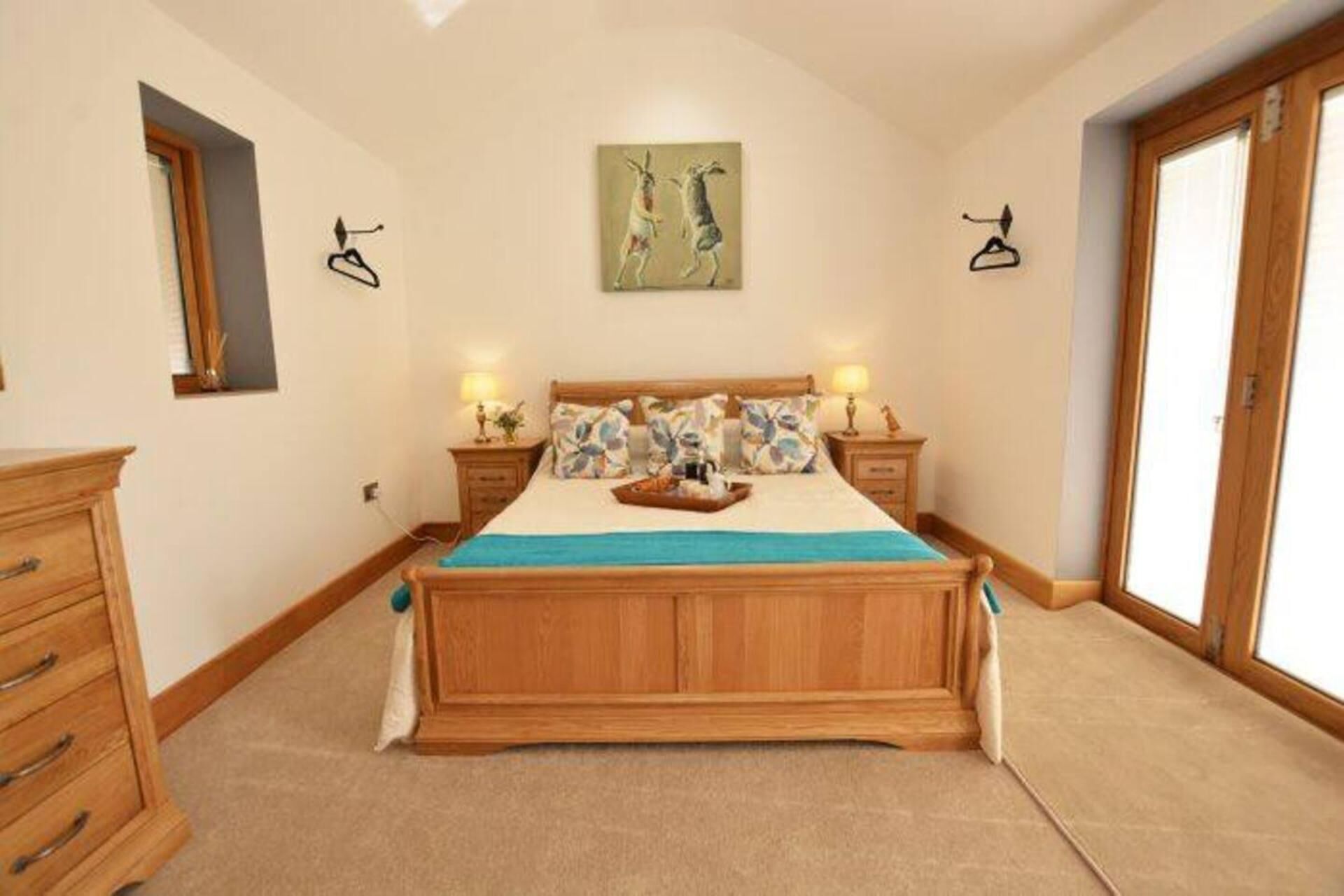 A bedroom with a wooden bed, two bedside tables with lamps, a large window, and a painting on the wall.