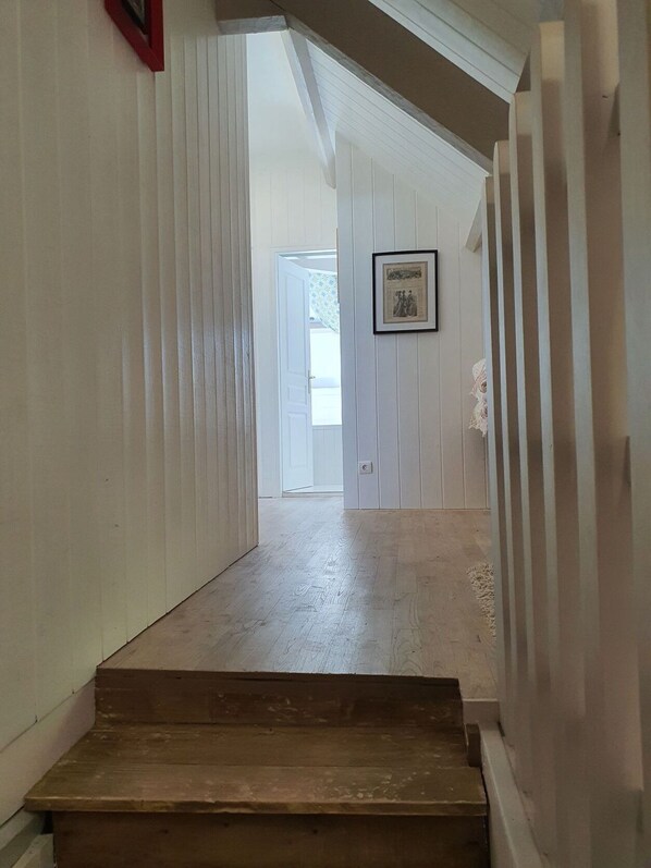 Una escalera de madera que conduce a una habitación con paredes blancas empapeladas y un cuadro enmarcado en la pared.