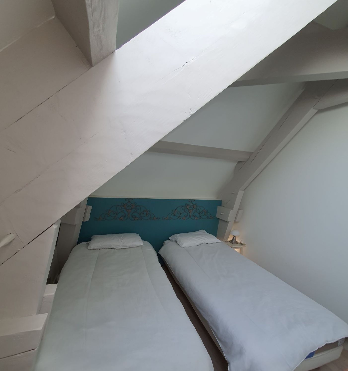 Een kleine, smalle kamer met twee eenpersoonsbedden, een blauw hoofdeinde en een schuine plafond.