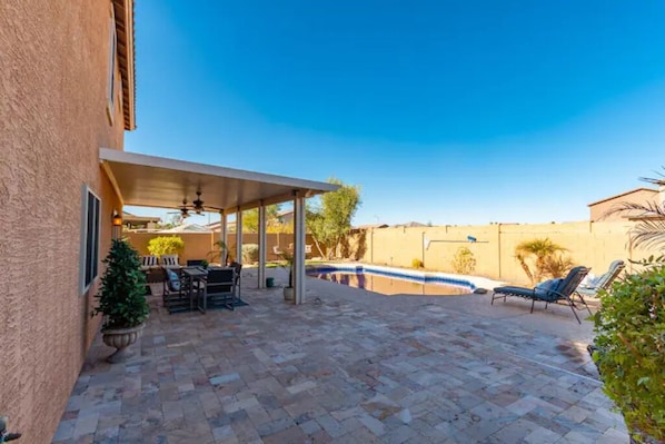 Eine überdachte Terrasse mit Pool, Gartenmöbeln und blauem Himmel.