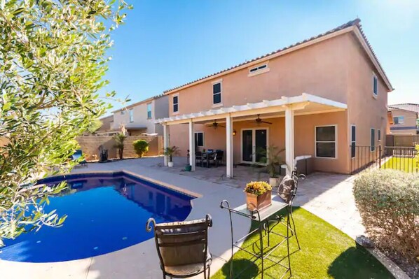 Une maison à deux étages dotée d’un patio couvert, d’une piscine et d’une pelouse bien entretenue.