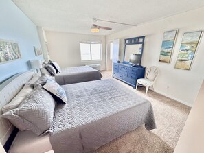A bedroom with two beds, a dresser, a chair, and artwork on the walls.
