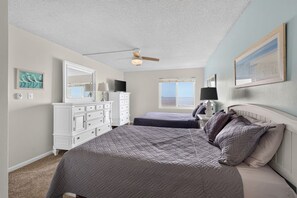 A bedroom with two beds, a dresser, a ceiling fan, and a window with a view.