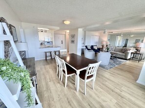 A spacious living area with a wooden dining table surrounded by chairs, a kitchen in the background, and a cozy seating area with a sofa and armchairs.