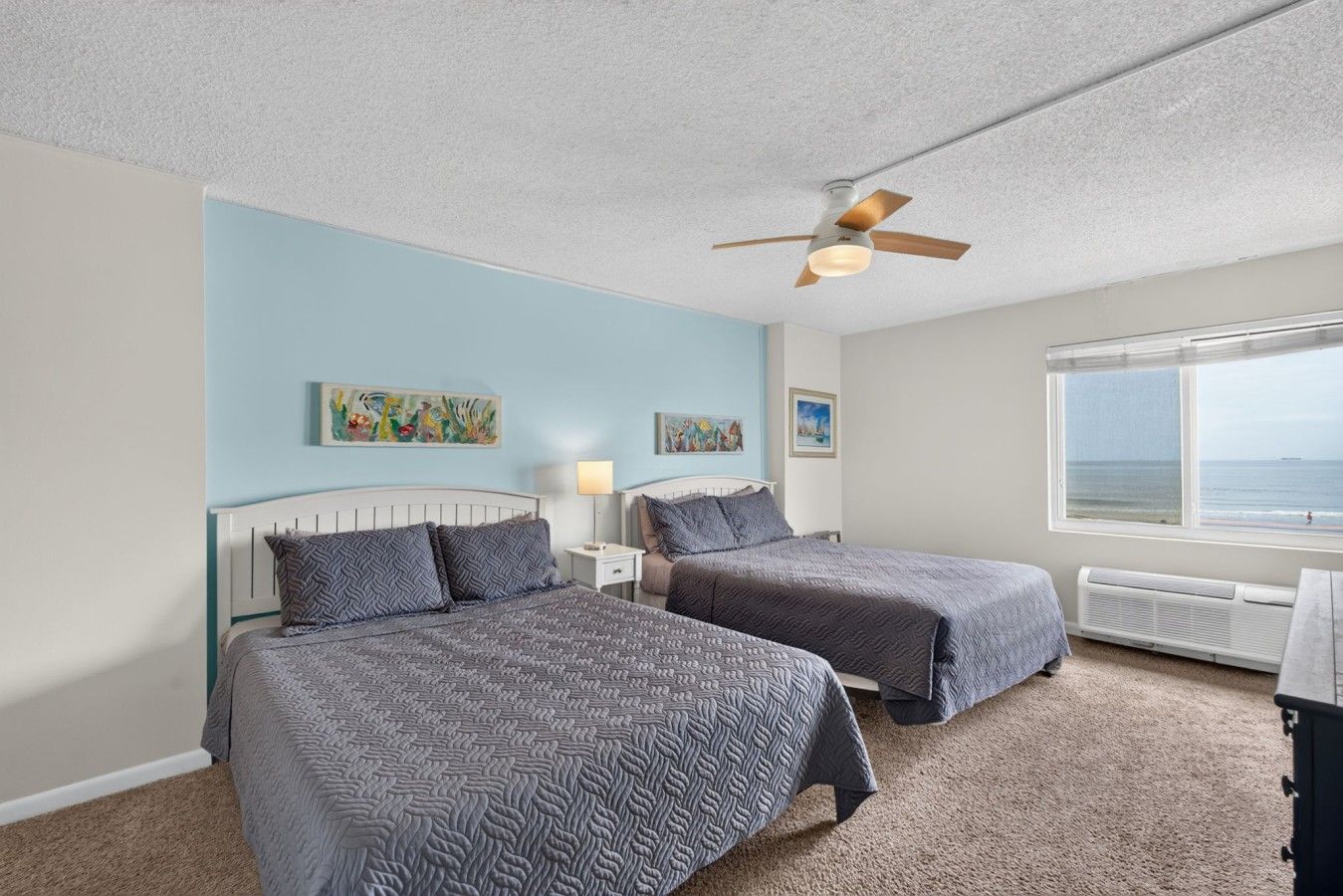 A bedroom with two beds, a ceiling fan, artwork on the walls, and a window with a view.