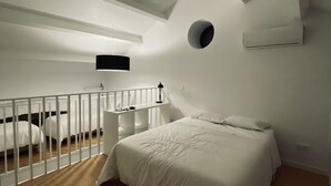 A bedroom with a sloped ceiling, a round window, a bed, a desk, and a white railing. - Old Railway Station in Evoramonte - House #1 (Evoramonte)