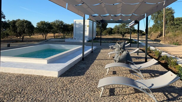 A pool area with lounge chairs under a canopy, surrounded by gravel and trees. - Old Railway Station in Evoramonte - House #1 (Evoramonte)