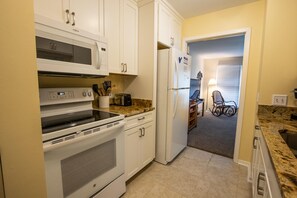 Kitchen area with oven, microwave, toaster, and refrigerator, adjacent to a dining space with a table and chair.
