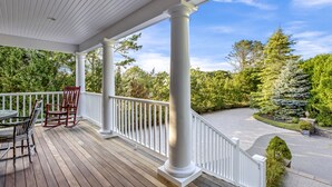 A covered porch with white railings and columns, a table, and two chairs. - Beautiful Southampton Home with breathtaking waterfront views, front porch,... (Southampton)