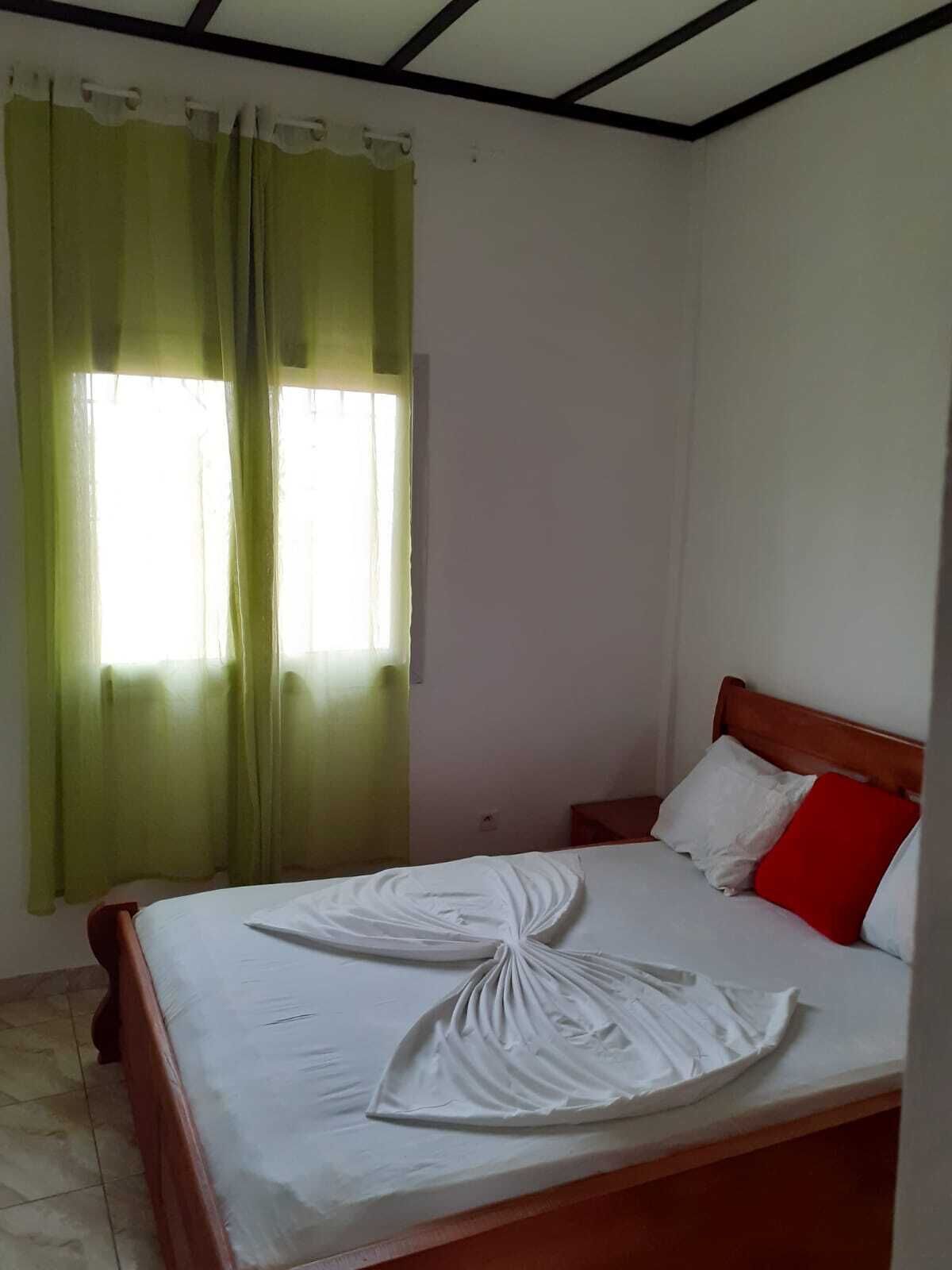A room with a bed, a wooden headboard, a green curtain, and a white wall.