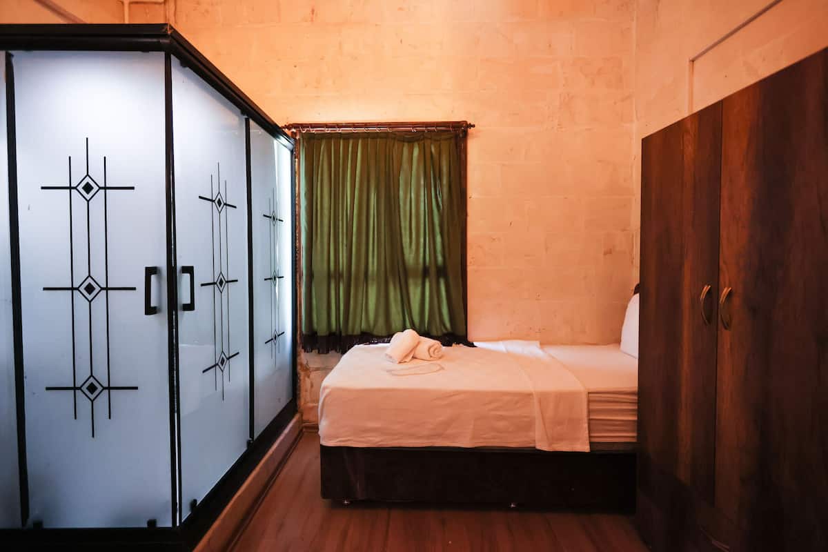 A small, neatly arranged bedroom with a bed, a wardrobe, and a green curtain.