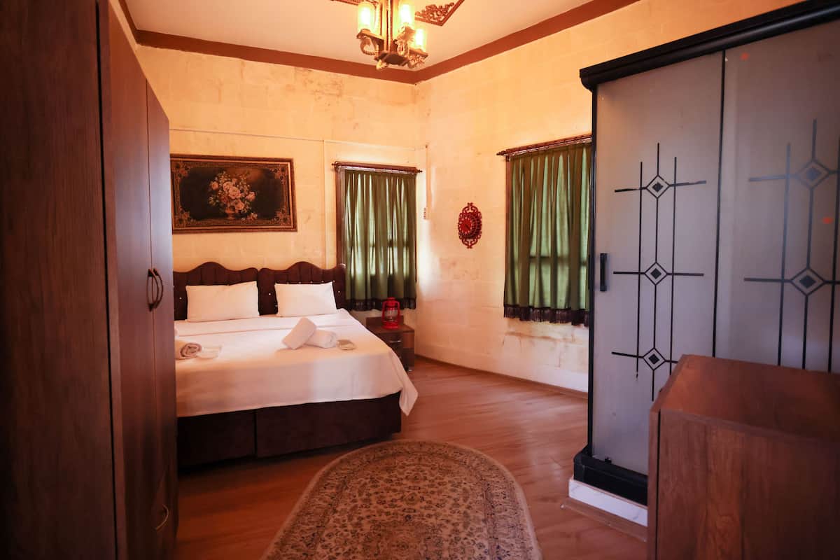 A bedroom with a bed, a wooden wardrobe, a nightstand, and a painting on the wall.