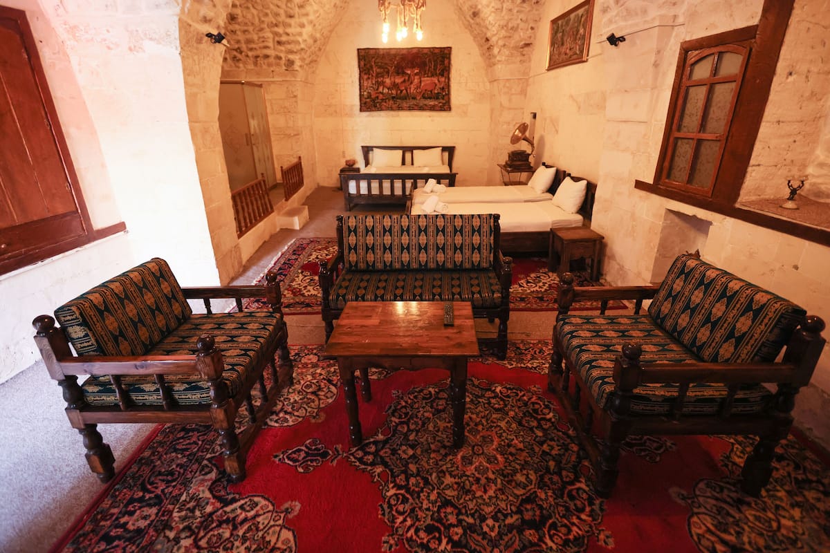 A traditional room with a stone wall, a bed, two sofas, a wooden table, and a patterned rug.