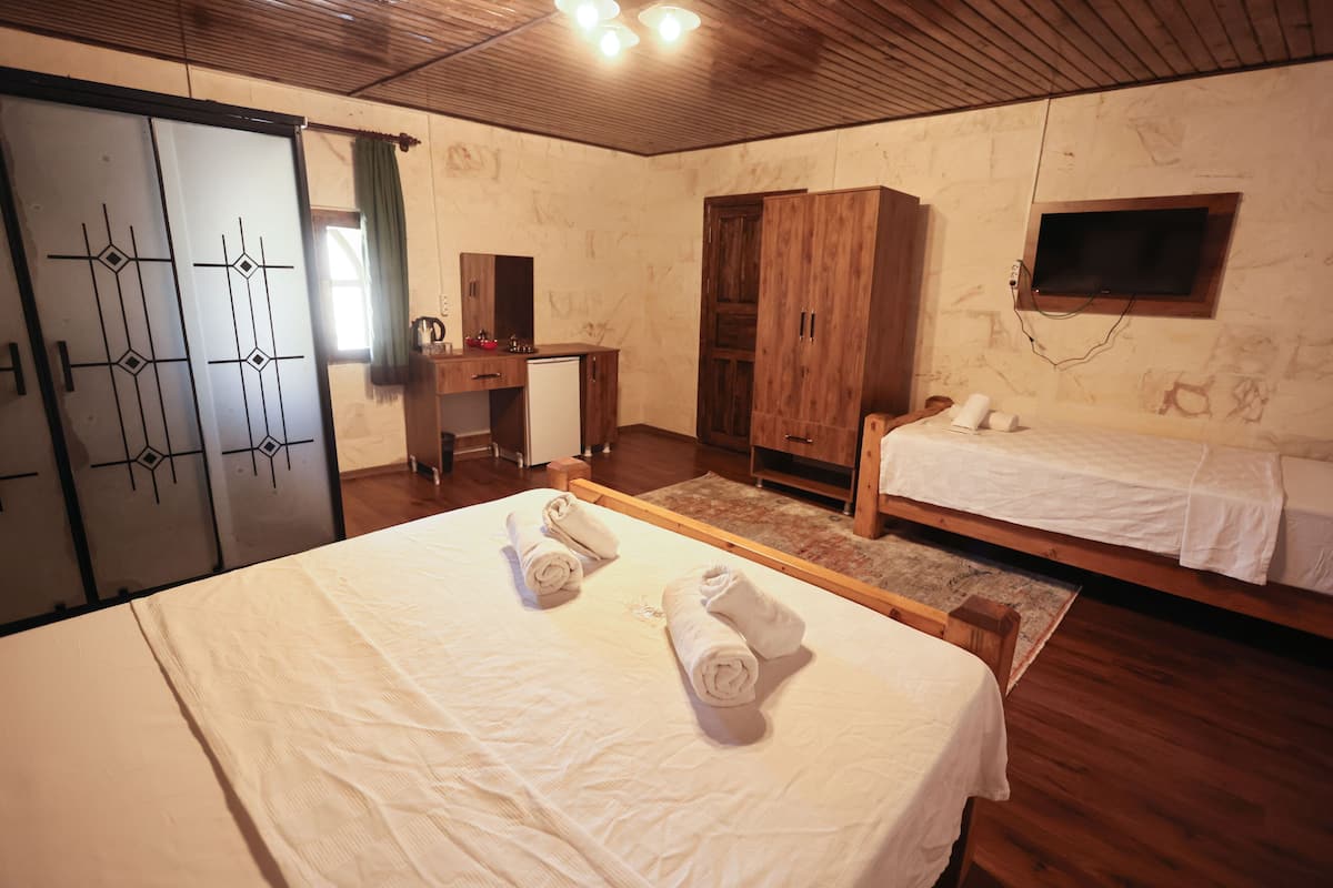 A bedroom with two beds, wooden wardrobe, a desk, and a television.
