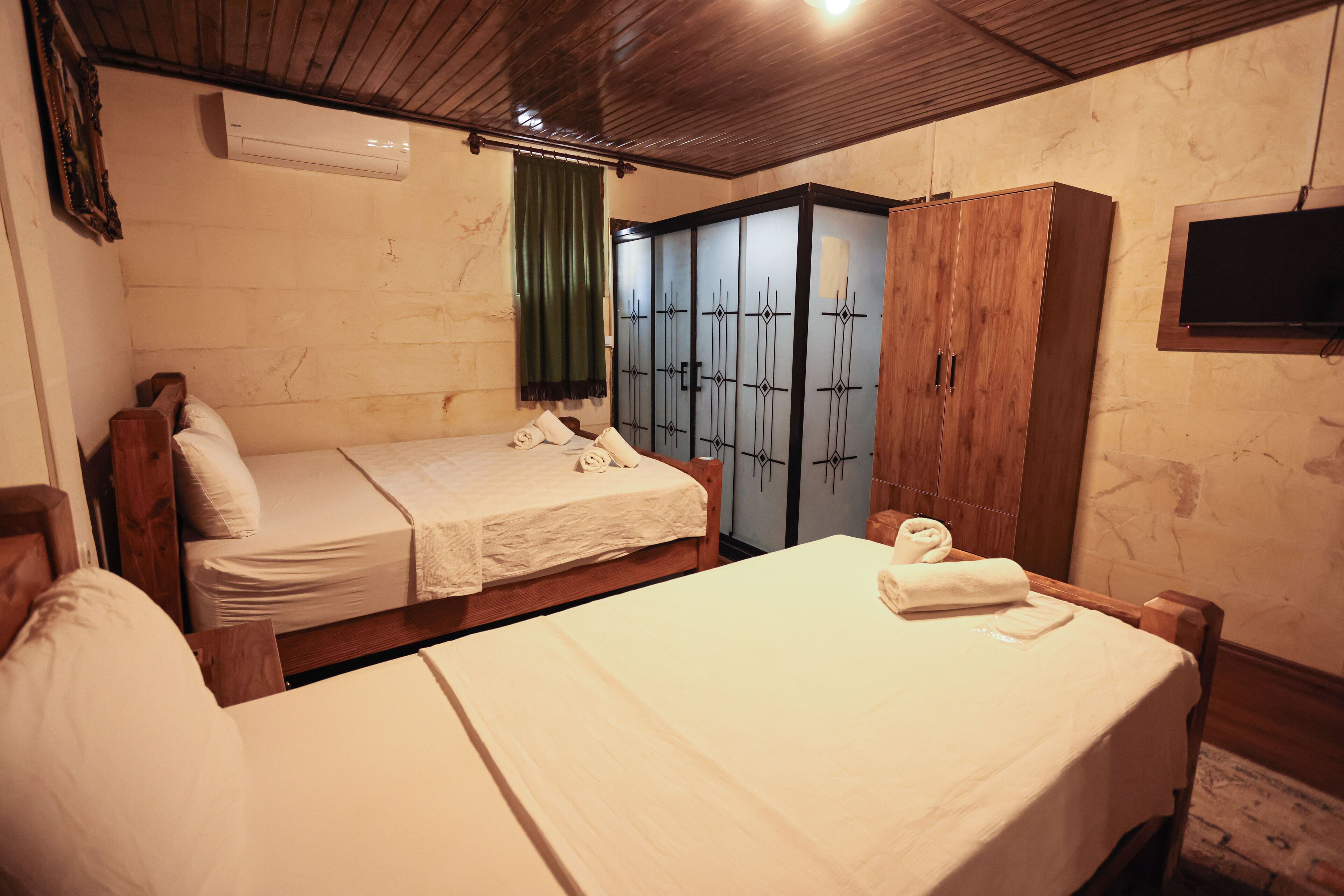 A room with two single beds, a wooden wardrobe, a television, and an air conditioning unit.