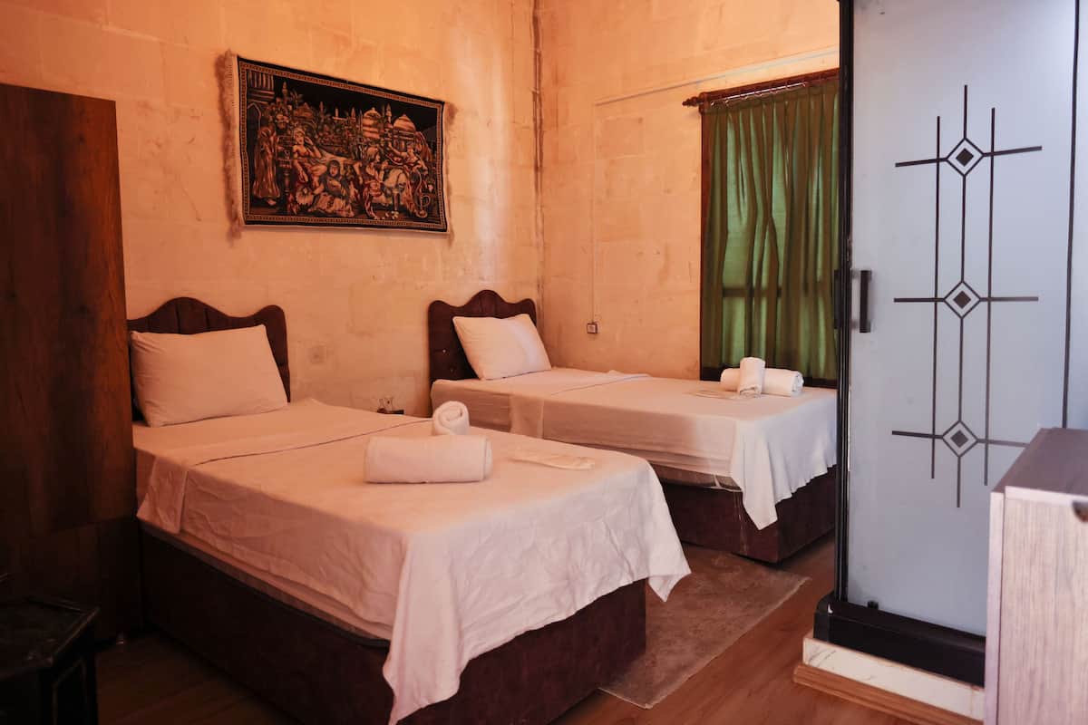 A room with two beds, each with a white bedspread and pillows, a painting on the wall, and a green curtain on the window.