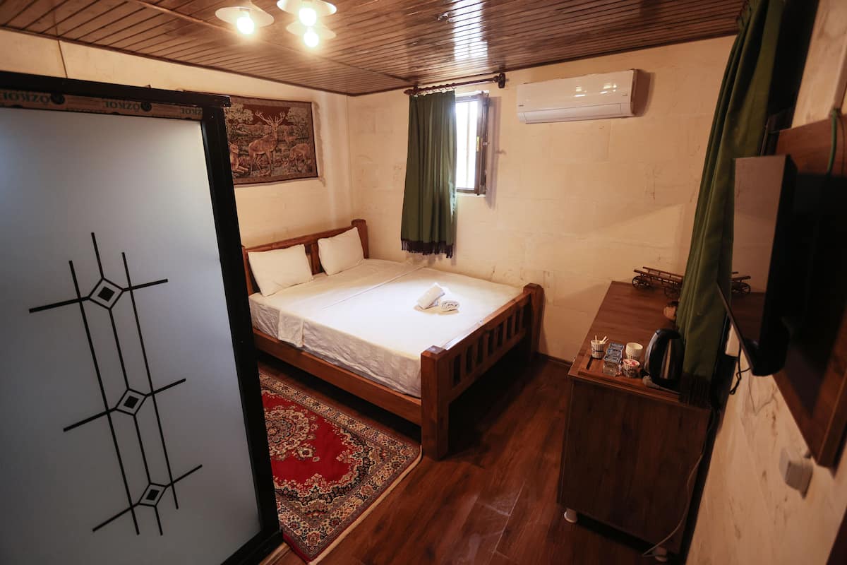 A bedroom with a wooden bed, a small desk, a red rug, and a white wall with a painting.