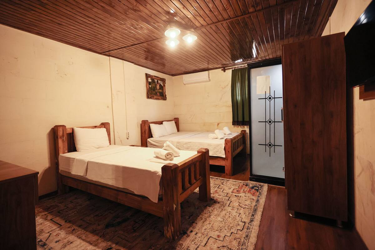 A room with two wooden beds, a wooden wardrobe, a patterned rug, and a painting on the wall.