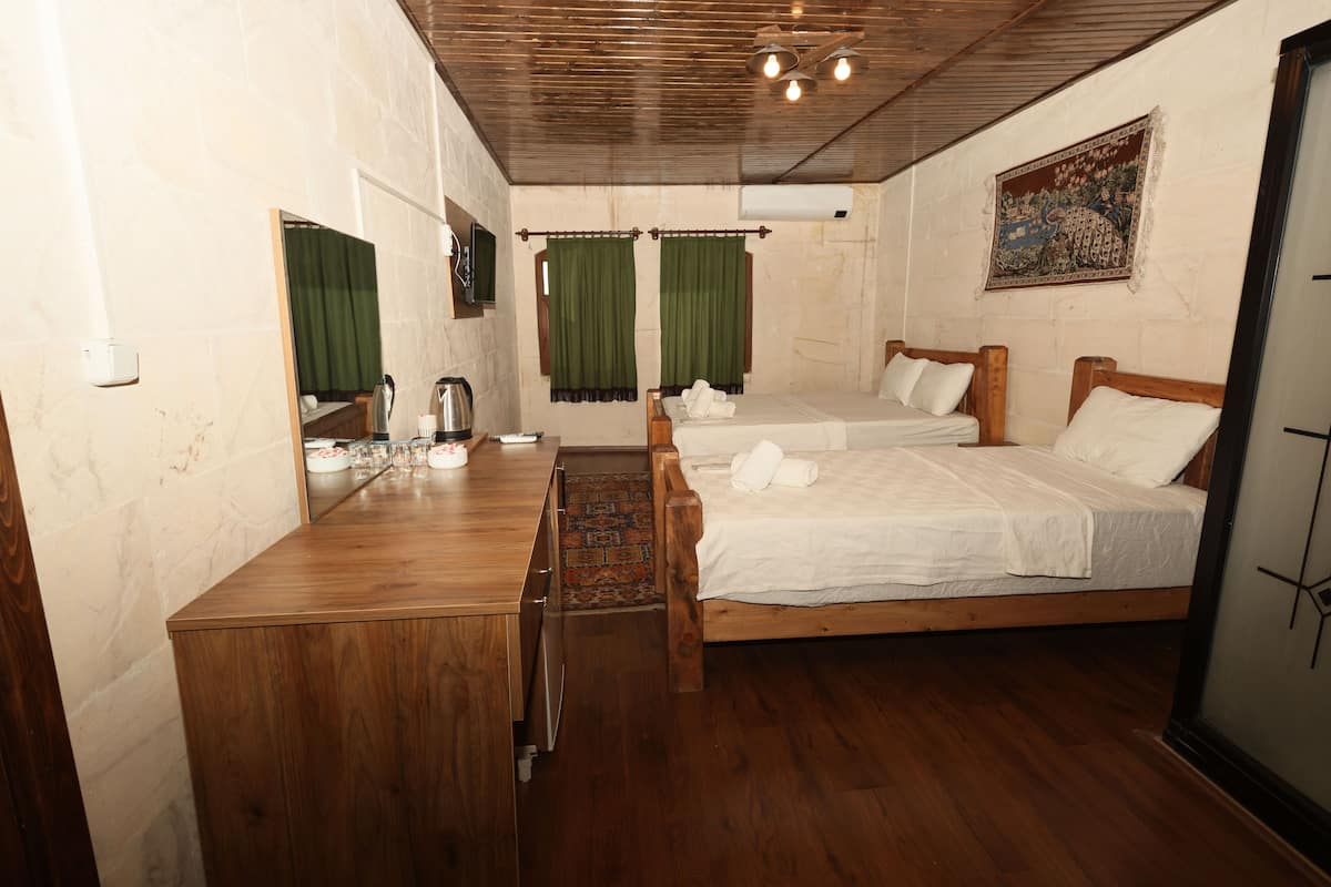 A hotel room with two wooden beds, a wooden desk, a mirror, a television, and a window with green curtains.