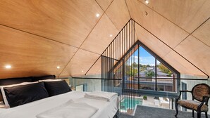 Ein modernes Schlafzimmer mit einem großen Bett, einem Sessel und Blick auf einen Swimmingpool durch eine Glaswand.
