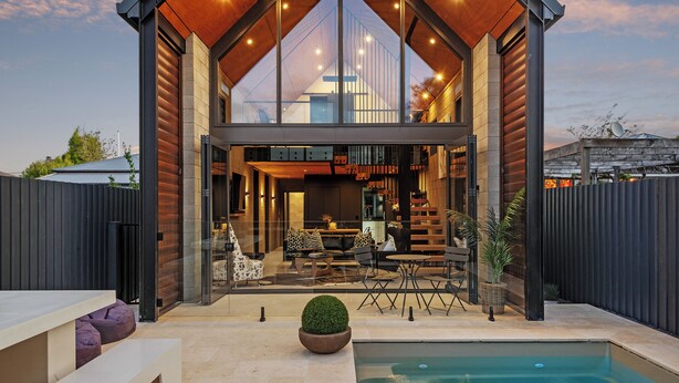 Ein modernes Haus mit großer Glasfront, einem Pool und Gartenmöbeln.