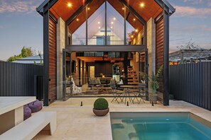 A modern house with a large glass front, a pool, and outdoor furniture. - Divine on Derby - Christchurch Holiday Home (Christchurch)