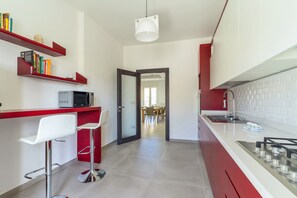 Una cucina moderna con mobili rossi e bianchi, un piano di lavoro bianco e un'area pranzo visibile attraverso una porta aperta.