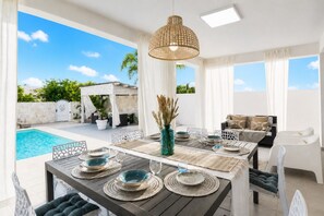 A dining area with a pool view, outdoor seating, and a pergola.