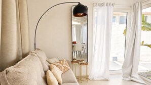 A living room with a sofa, pillows, a mirror, a lamp, and a view through a window. - Villa Soave SicilyMyHome (Santa Maria del Focallo)