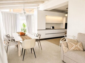 A modern kitchen with white cabinetry, a dining table with chairs, and a sofa with a patterned throw.
