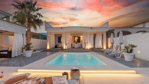 A modern pool area with a sunset sky, a dining area with white curtains, and lounge chairs. - Villa Soave SicilyMyHome (Santa Maria del Focallo)