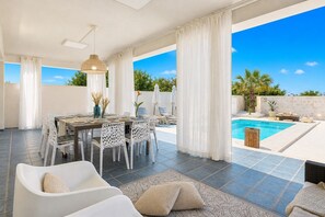 Un amplio espacio exterior con mesa, sillas, lámpara colgante, piscina y vista al cielo.