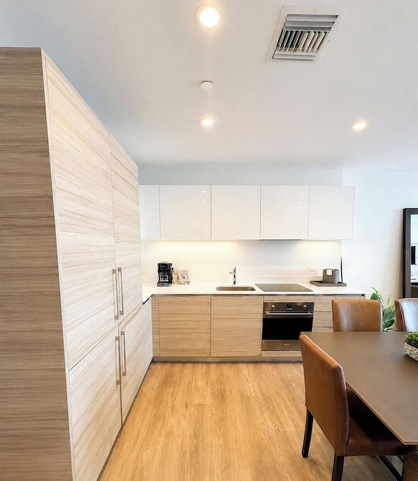 A modern kitchen with light wood cabinetry, a stainless steel sink, and a dining area with a table and chairs.