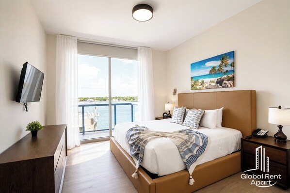Habitación de hotel con cama, televisor, balcón con vista al mar y un cuadro en la pared.