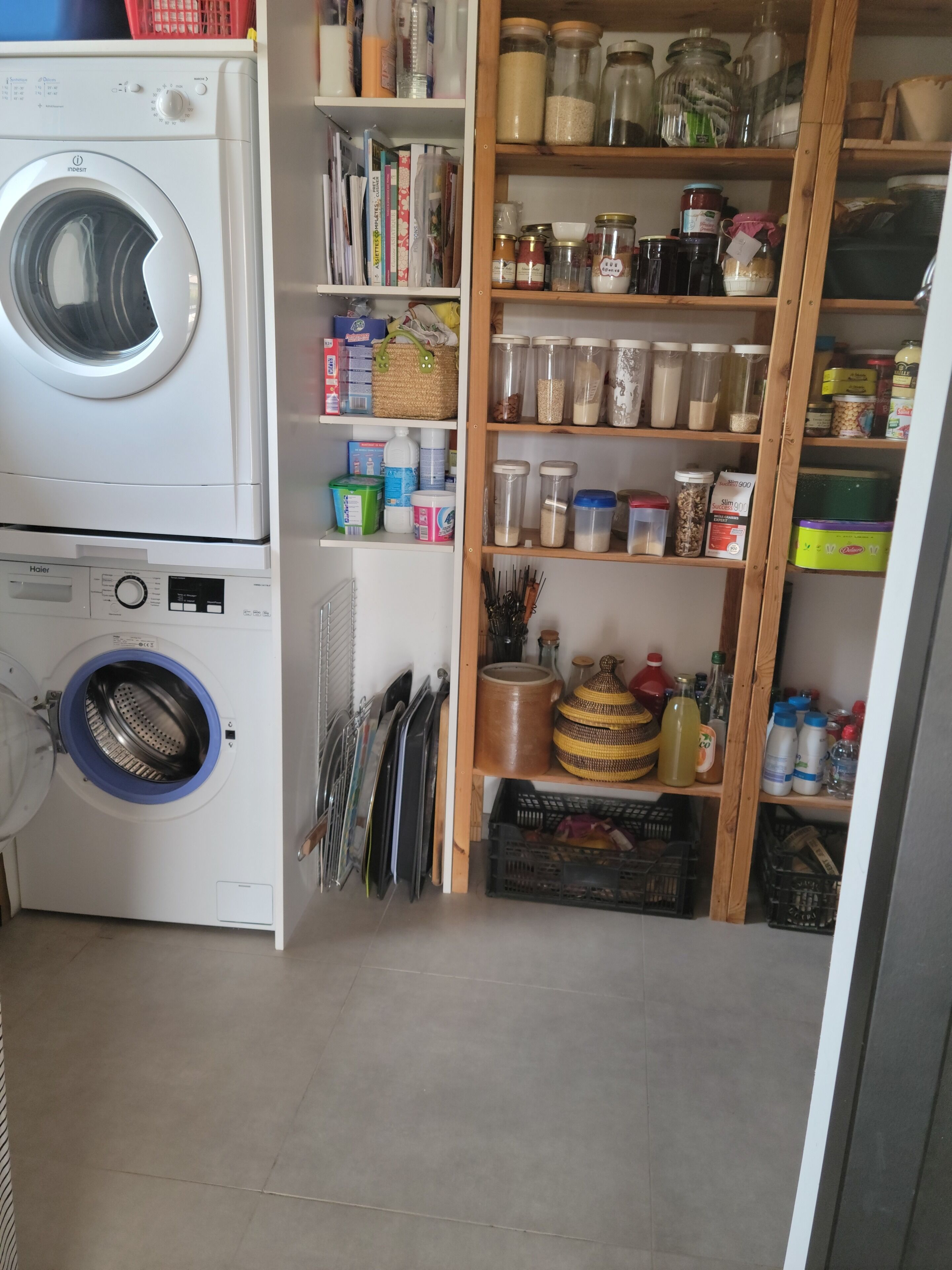 A laundry area with a front-loading washing machine and a dryer, shelves with storage jars, and a variety of kitchen utensils.